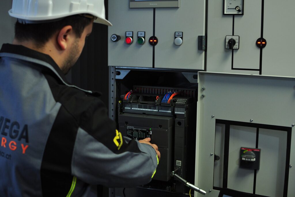 Techniker mit Schutzhelm bedient einen Leistungsschalter in der geöffneten Schaltanlage