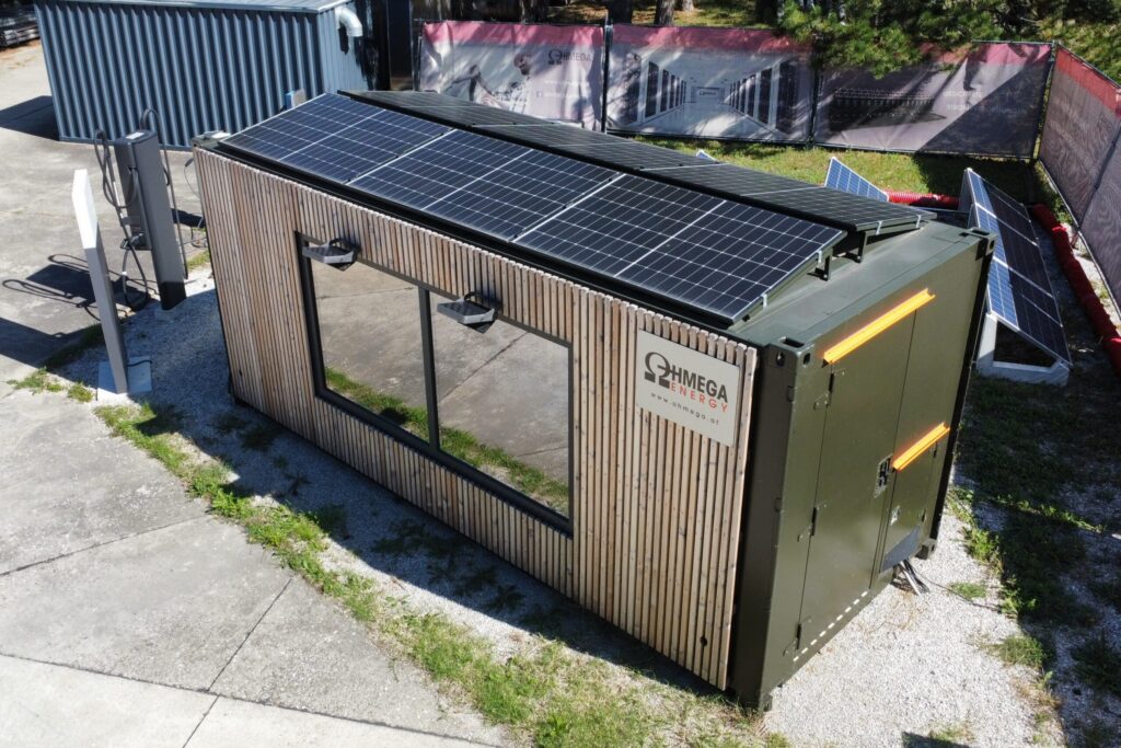 Mobiler Energiespeicher-Container mit Holzfassade und Solarmodulen auf dem Dach, daneben eine Ladesäule