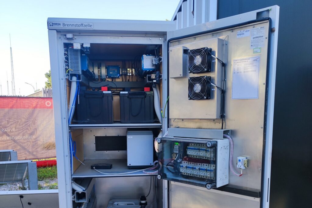Geöffneter Schaltschrank Brennstoffzelle mit Batterieblöcken, Lüftern und Sicherungsautomaten im Freien